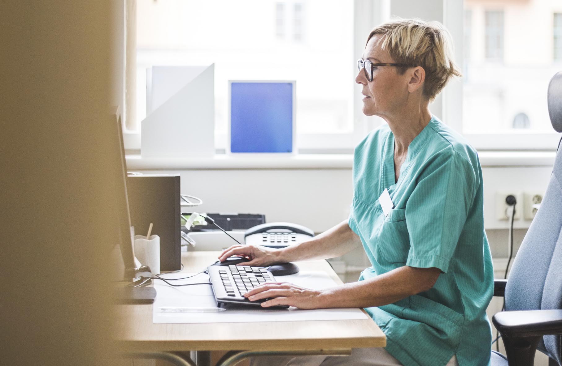 Side view of mature doctor working over computer while sitting in clinic