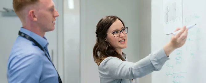 Kvinna ritar på en whiteboard medans en man som står bakom henne iaktar