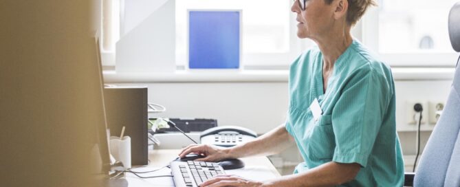 Side view of mature doctor working over computer while sitting in clinic